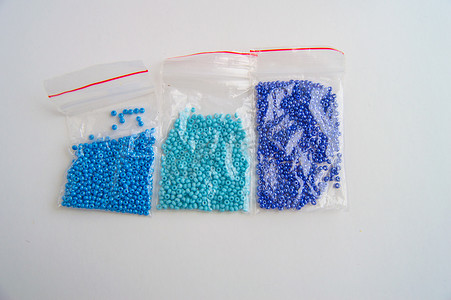 渐变色摄影照片_一组三个塑料袋，蓝色玻璃珠，白色背景渐变色，珠绣配件