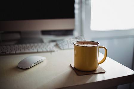 在阳光明媚的晨光中，办公桌上放着一杯黄色的咖啡，旁边是显示器和键盘