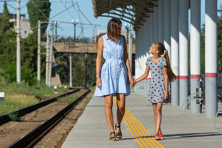 站台上摄影照片_年轻漂亮的女孩和十几岁的女儿走在火车站空荡荡的站台上