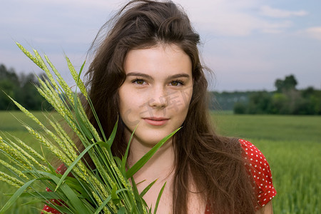 美丽的女孩在绿地里穿红裙子，带着一束麦子