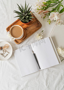 在白色床上打开书本、咖啡和鲜花的顶视图。