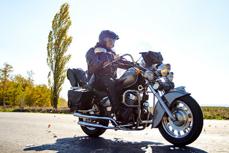摩托车背景摄影照片_摩托车司机在秋季公路上骑着定制的斩波自行车。