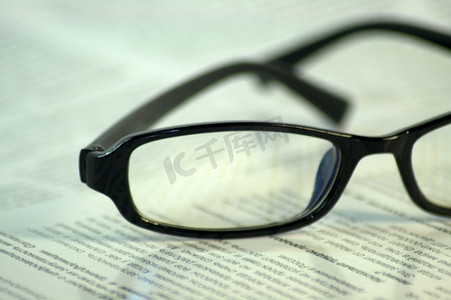 新闻报纸框摄影照片_黑框眼镜躺在杂志的页面上。