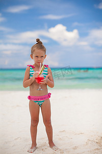 小女孩在异国情调的海滩上喝西瓜汁