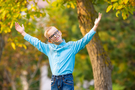 热闹的七岁男孩在秋季城市公园兴高采烈地举起双手