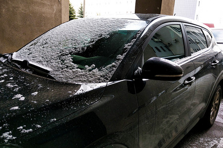 挡风玻璃摄影照片_汽车的挡风玻璃上覆盖着薄薄的雪。