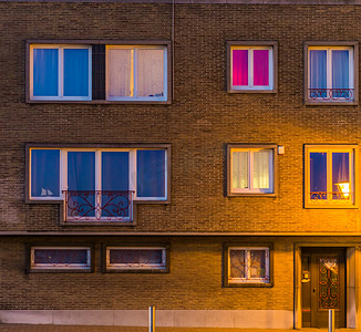 夜间照明的公寓大楼、比利时住宅、带窗户和前门的建筑外墙