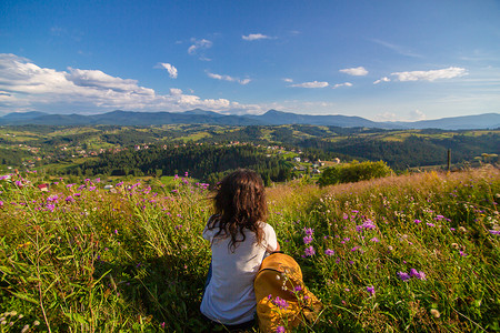 叹为观止摄影照片_快乐的美女坐在山上的花田里欣赏山景，欣赏令人叹为观止的自然景观