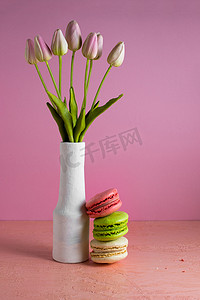 背景淡粉摄影照片_淡粉色背景上的蛋白杏仁饼干，旁边是一瓶郁金香。