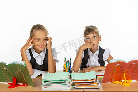 对话题框摄影照片_两个女孩坐在学校的课桌前思考一个抽象的话题