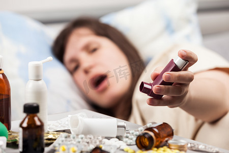 卧病在床摄影照片_卧病在床的女病人手里拿着哮喘吸入器