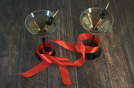 两杯加橄榄的马提尼酒杯，木桌上系着一条猩红色丝带。