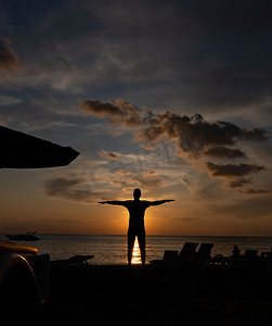 一个男人张开双臂站在夕阳下的剪影。