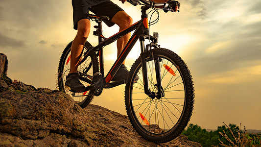 骑山地自行车的骑自行车者在日落时分在岩石下。