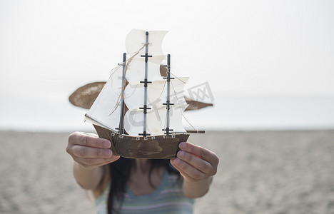 玩具帆船摄影照片_女人在沙滩上拿着船模型