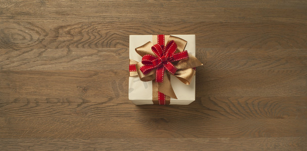 金色蝴蝶结摄影照片_木桌上系着红色和金色蝴蝶结的圣诞礼盒
