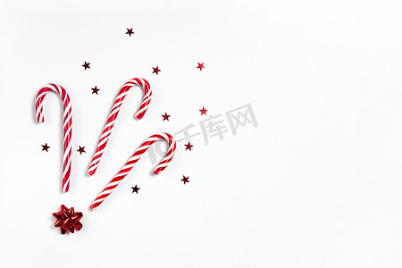 圣诞作文三个焦糖棒棒糖、五彩纸屑星和白色背景上的红色蝴蝶结，带有复制空间。