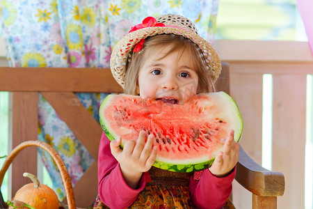 戴着草帽的小女孩胃口大开，吃着成熟的西瓜