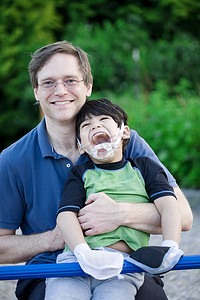 保姆抱孩子摄影照片_父亲在操场上抱着残疾的儿子