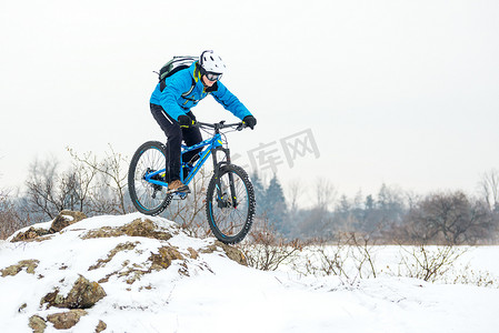 蓝色骑山地自行车的骑自行车者在覆盖着雪的岩石冬季山上。