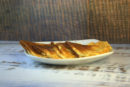 陶瓷盘子上的四个新鲜煎饼躺在一张木桌上。