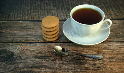 木桌上放着一杯放在瓷碟上的红茶、一把勺子和一堆巧克力海绵饼干。