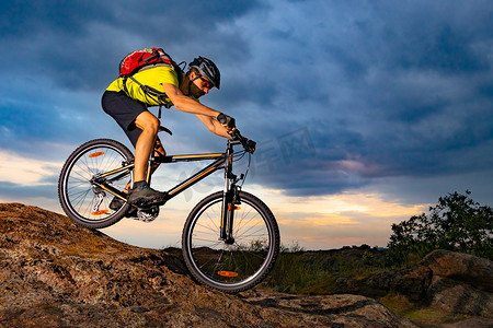 山地自行车摄影照片_骑山地自行车的骑自行车者在日落时在岩石小道上骑山地自行车。