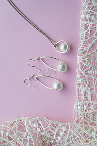 漂亮的银色闪亮珍珠首饰，时尚迷人的耳环，粉色紫色背景上的链条，配以精致的蕾丝。