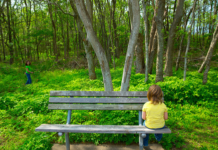孤独的孩子悲伤地看着森林坐在长椅上