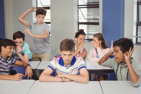 欺负人摄影照片_学校朋友在教室里欺负一个悲伤的男孩