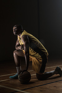 篮球运动员的肖像，膝盖放在地板上，一只手放在球上，向上看