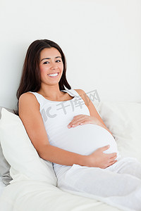 摸着肚子摄影照片_一位漂亮孕妇躺在床上摸着肚子的正面图