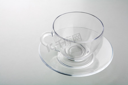 透明灰色背景摄影照片_在灰色隔离的盘子上的杯子