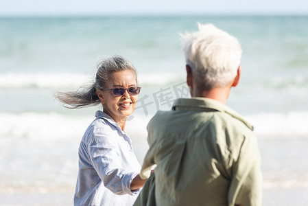 高级男女夫妇手牵着手走到阳光明媚的海滩，蓝天明媚