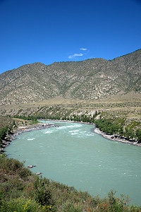 卡通景色摄影照片_位于高岩石山脚下的山谷中，一条绿​​松石色的山区河流的河道弯曲。