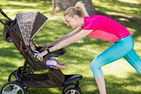 着婴儿车的妈妈在公园里聊天双肩包儿童推车一对夫妇推着婴儿车在公园