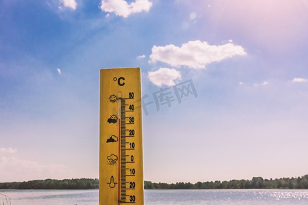 显示 30 摄氏度热量的温度计以湖水和蓝天为背景在阳光下
