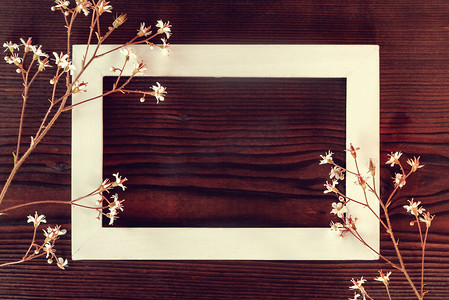 深色木质背景上的白色木框，上面有小花 — 贺卡或邀请函的模板