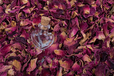 可爱瓶瓶摄影照片_在干燥玫瑰花瓣背景的空的瓶