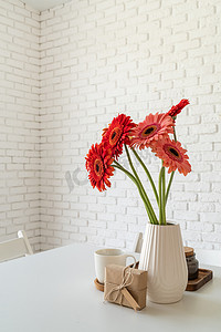 厨房桌上白色花瓶中明亮的非洲菊雏菊，带礼盒，风格极简