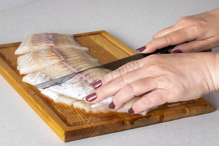 女手在砧板上用刀切鱼肉。