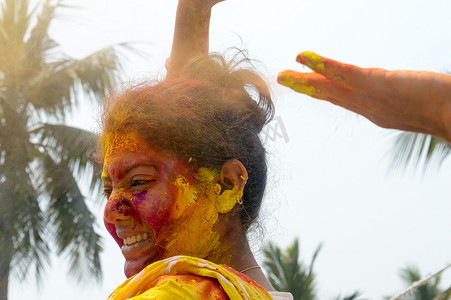 在 Holi 色彩节期间，一位年轻的印度快乐女人的肖像，脸上涂着粉红色、黄色和红色的 Holi 彩色粉末涂料。