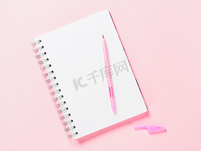 粉红色背景上带笔的空白笔记的顶部视图