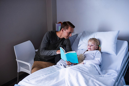 在医院病床上看书的女孩和她的父亲