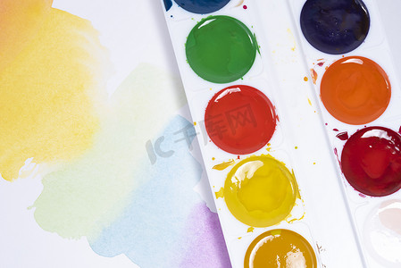 五颜六色的水彩笔触、画笔调色板的顶视图和带白纸的水彩颜料