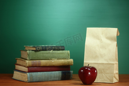 堆叠书籍摄影照片_教师桌上的书籍、苹果和午餐