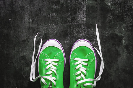 黑暗系背景摄影照片_蓝色-青色-绿色-绿松石色运动鞋，深色混凝土背景上系着不系带的鞋带。