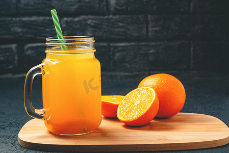 用橙子新鲜制作的柑橘汁，放在罐子里，杯子里放着灰色桌子上的吸管