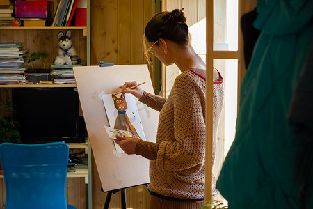 这位艺术家在靠窗的小作坊里，用丙烯颜料在画架上画了一幅猫的图画