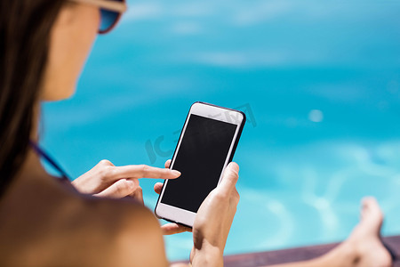 黑发女郎在池畔使用智能手机